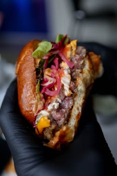 A flavorful gourmet burger with toppings held by a black-gloved hand, showcasing juicy ingredients.