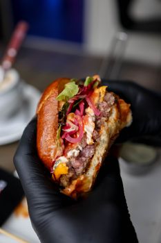 Close-up of a gourmet beef burger being held by gloved hands in a restaurant setting.