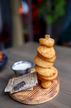 A delicious tower of crispy onion rings served with a side of creamy dip on a rustic wooden plate.