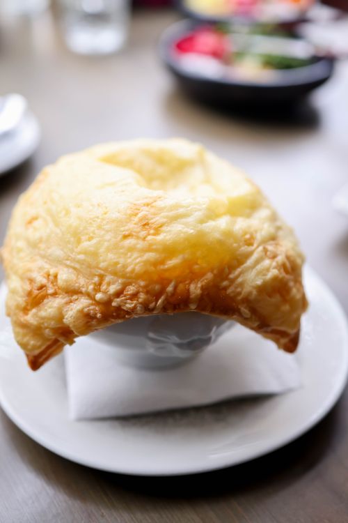 Free A delicious golden pastry covers a bowl, highlighting a fine dining experience with blurred ingredients in the background. Stock Photo