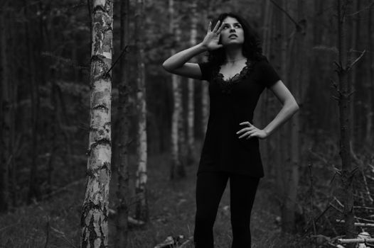 Elegant black and white portrait of a woman posing thoughtfully in a forest setting.