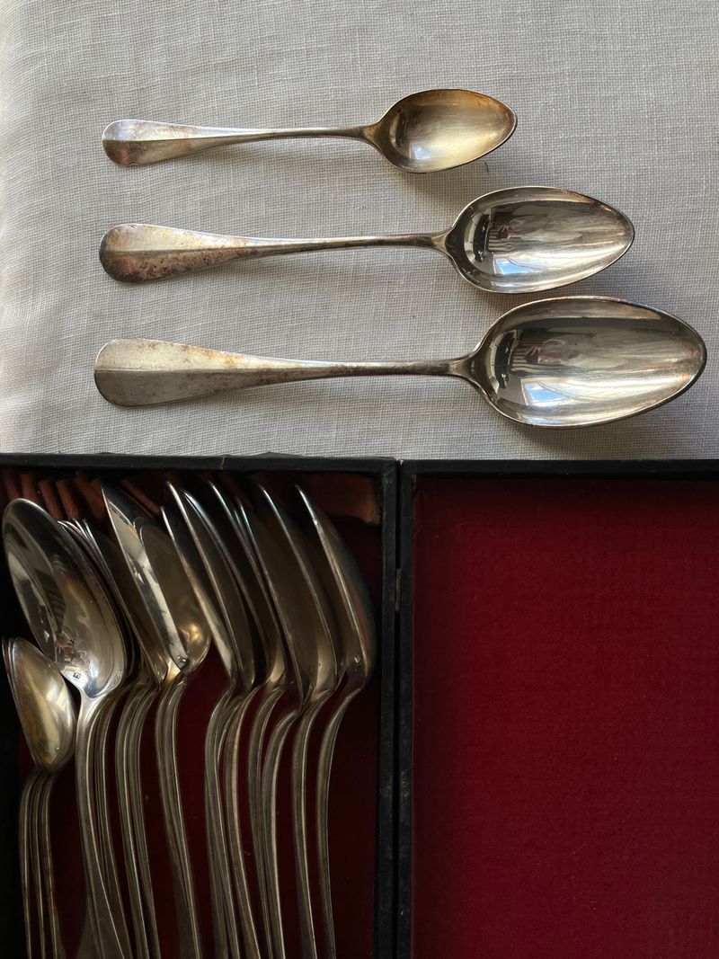 Tarnished antique silver spoons showing dark black oxidation in crevices, hallmark areas, and engravings — the characteristic silver sulphide tarnish of genuine sterling silver
