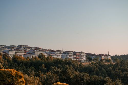 Free A picturesque townscape at sunset with buildings silhouetted against the sky and vibrant trees in the foreground. Stock Photo