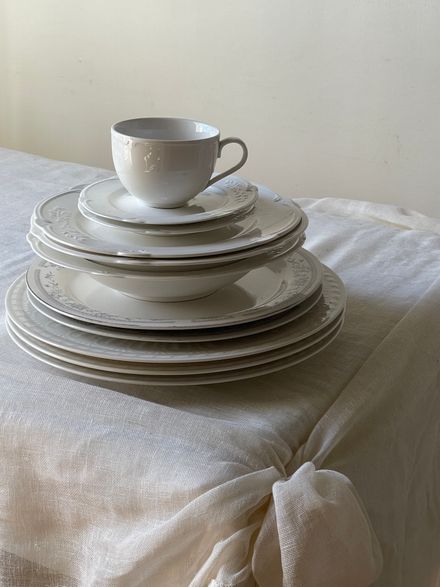 Stacked porcelain plates and a cup on draped linen — photo by Eugenia Remark on Pexels