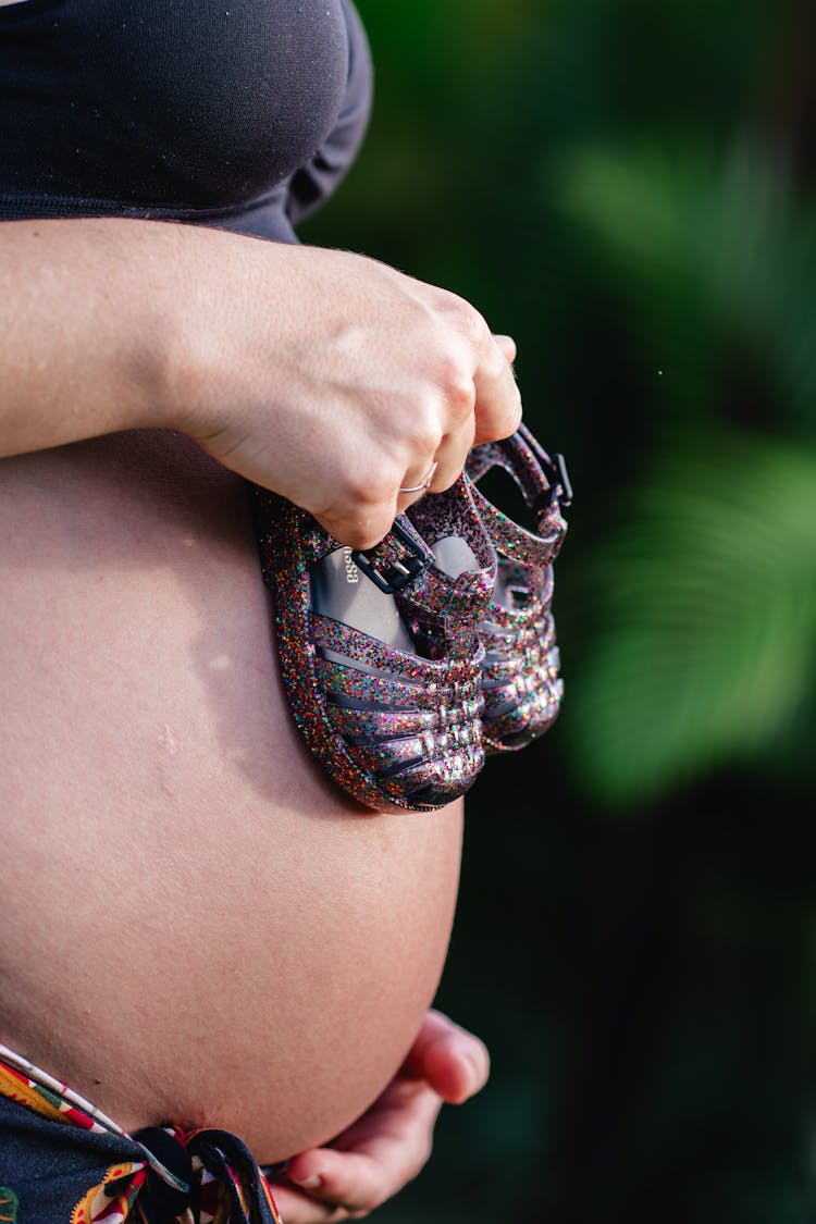 Pregnant Woman Hand Holding Baby Shoes