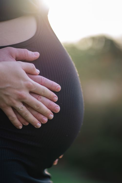 Free Close-up of a couple tenderly cradling a pregnant belly in soft light, symbolizing love and anticipation. Stock Photo