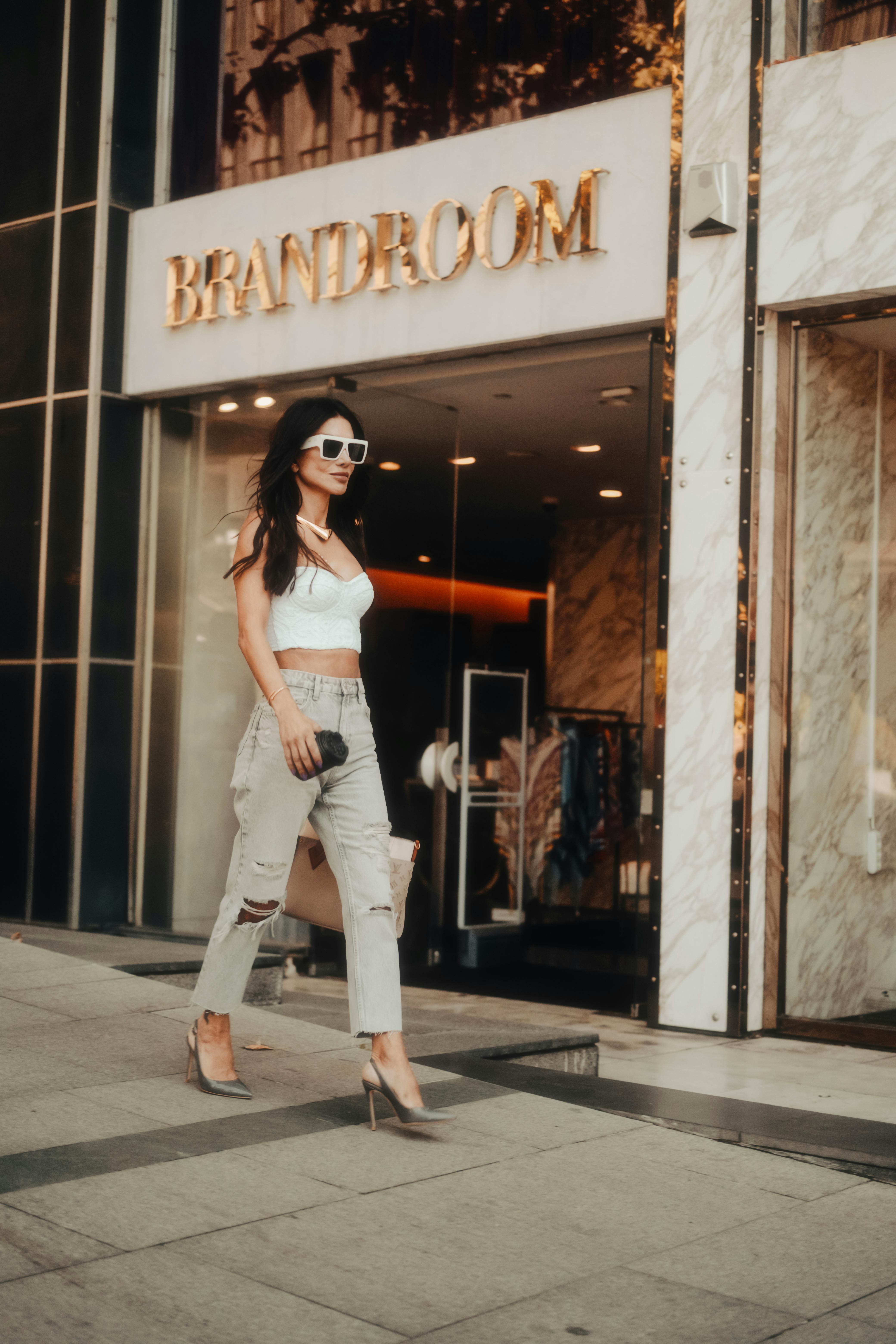 Model in a White Crop Top Gray Distressed Jeans and High Heels Walking in  Front of the Brandroom Boutique · Free Stock Photo