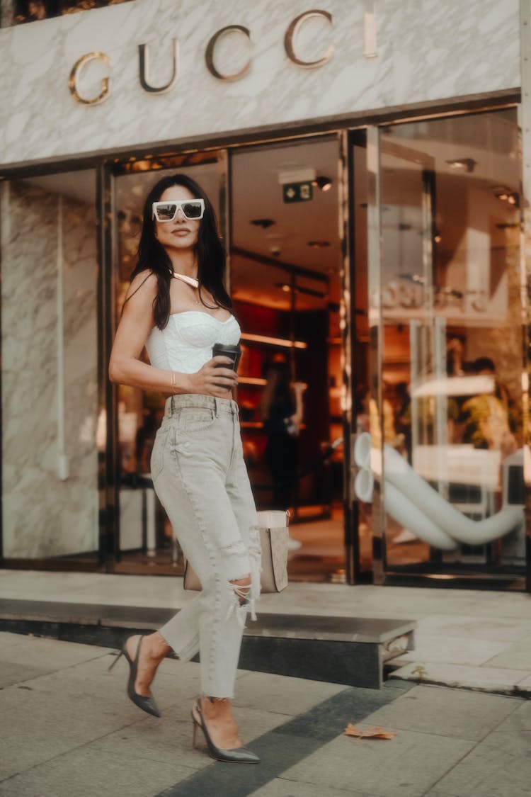 Model In A White Crop Top And Gray Distressed Jeans In Front Of A Gucci Store