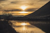 平静的河面上映着金色的日落，四周环绕着树木和山丘的剪影