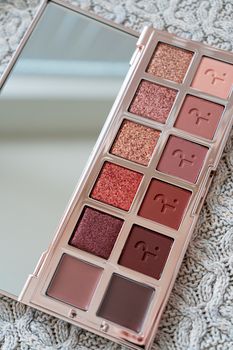 A sophisticated makeup palette with diverse eye shadow shades on a knitted surface.
