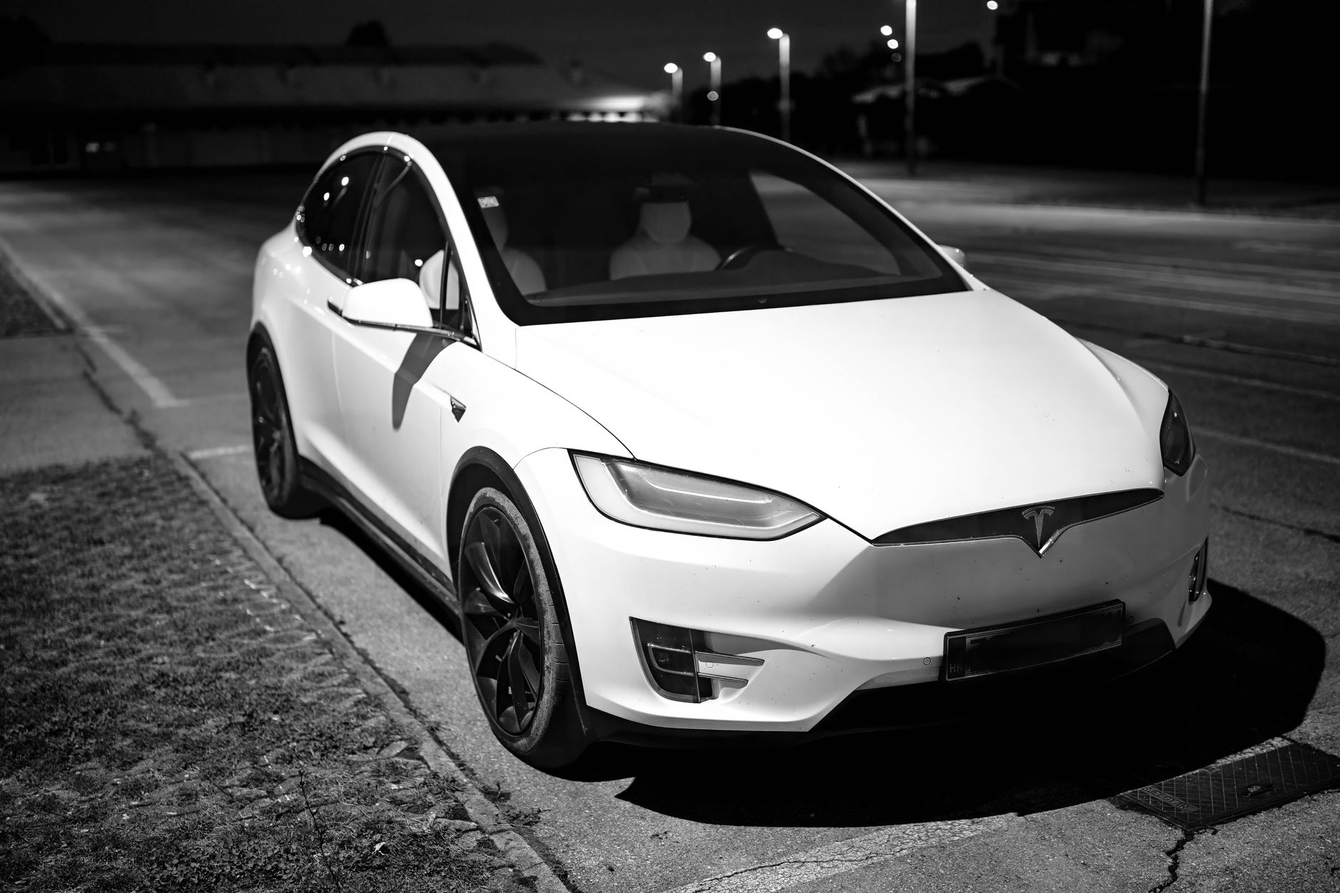 Black and white photo of a sleek white electric car parked on a dimly lit street at night.