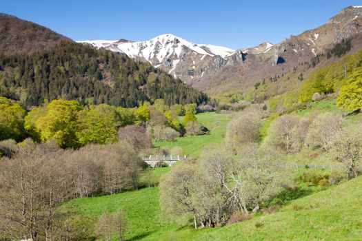 Beautiful landscape of Le Mont-Dore, France with snow-capped mountains and lush green valley in spring.