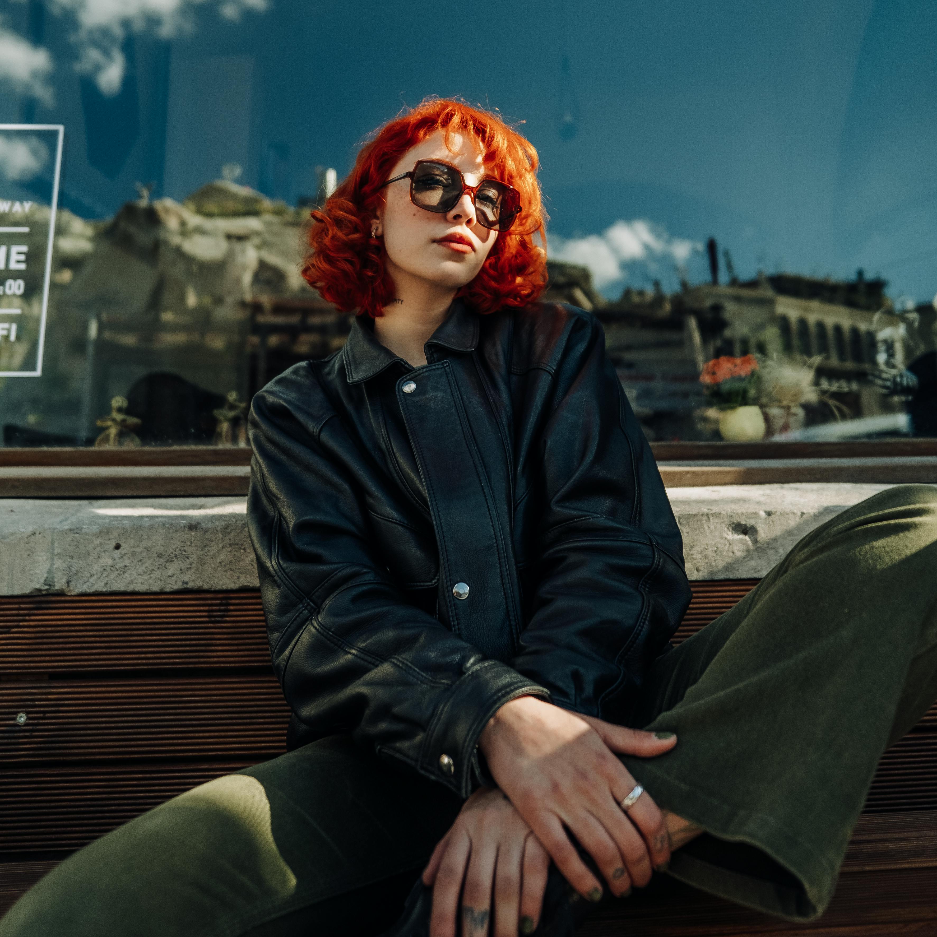 Young Redhead in a Leather Jacket and Sunglasses Sitting on a