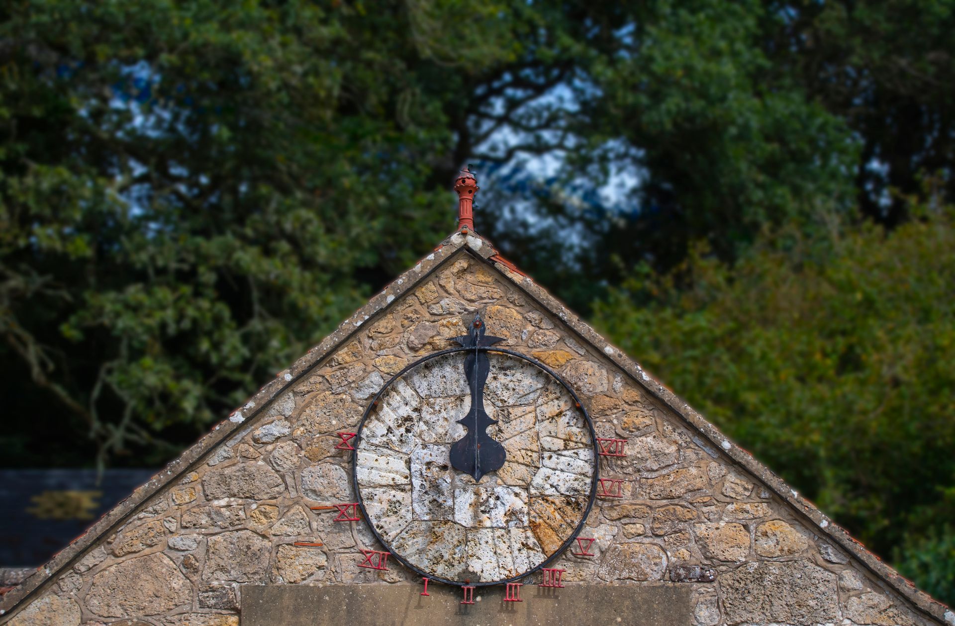 A vintage sundial on an old stone building against a lush, green background.