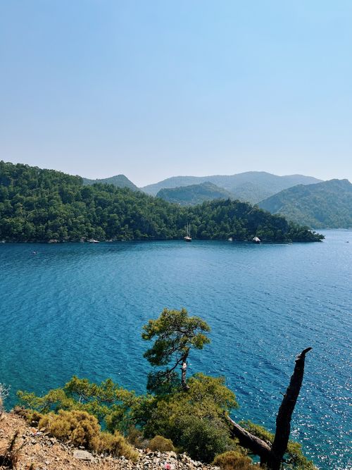Free Beautiful lake surrounded by lush green hills, clear blue waters, and sailboats on a sunny day. Stock Photo
