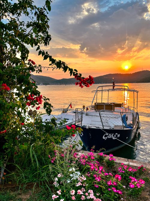 Free A tranquil scene of a boat anchored by a vibrant flower garden at sunset, capturing the essence of relaxation. Stock Photo