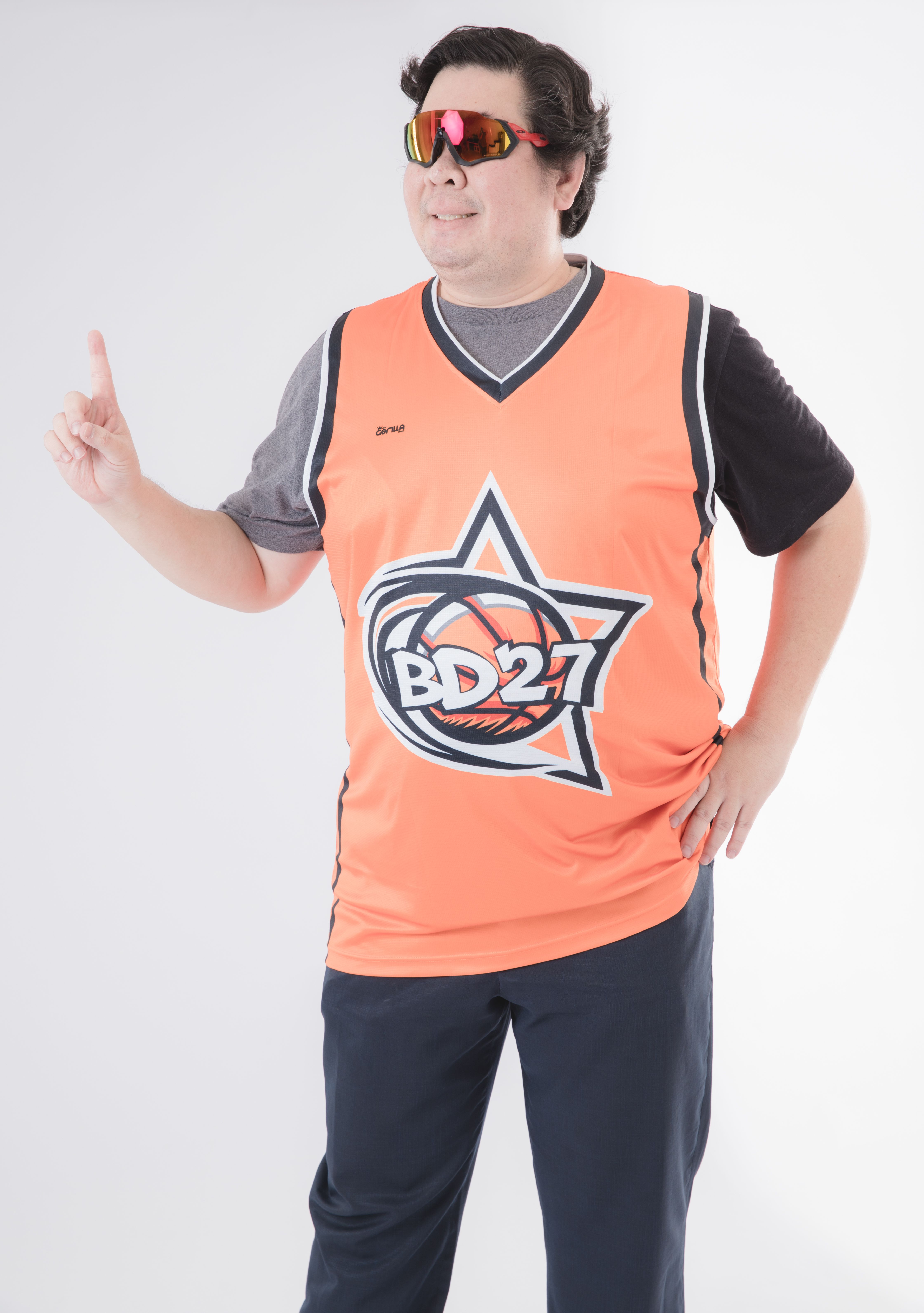 Man wearing orange sports jersey and sunglasses posing indoors with a confident gesture.