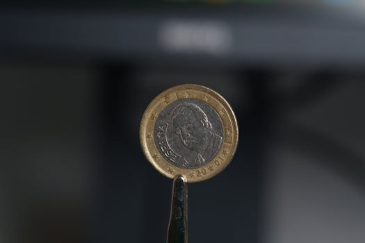 Close-up of a 2 Euro coin held with tweezers against a blurred background.