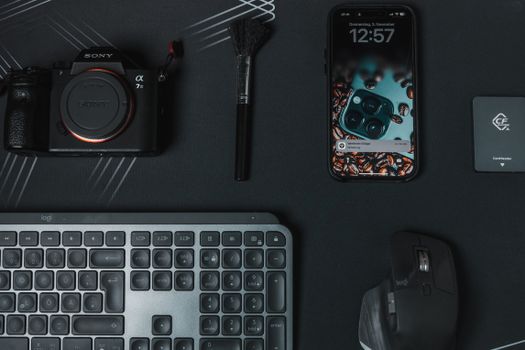 Flat lay of modern electronics including a camera, smartphone, and keyboard on a stylish black surface.