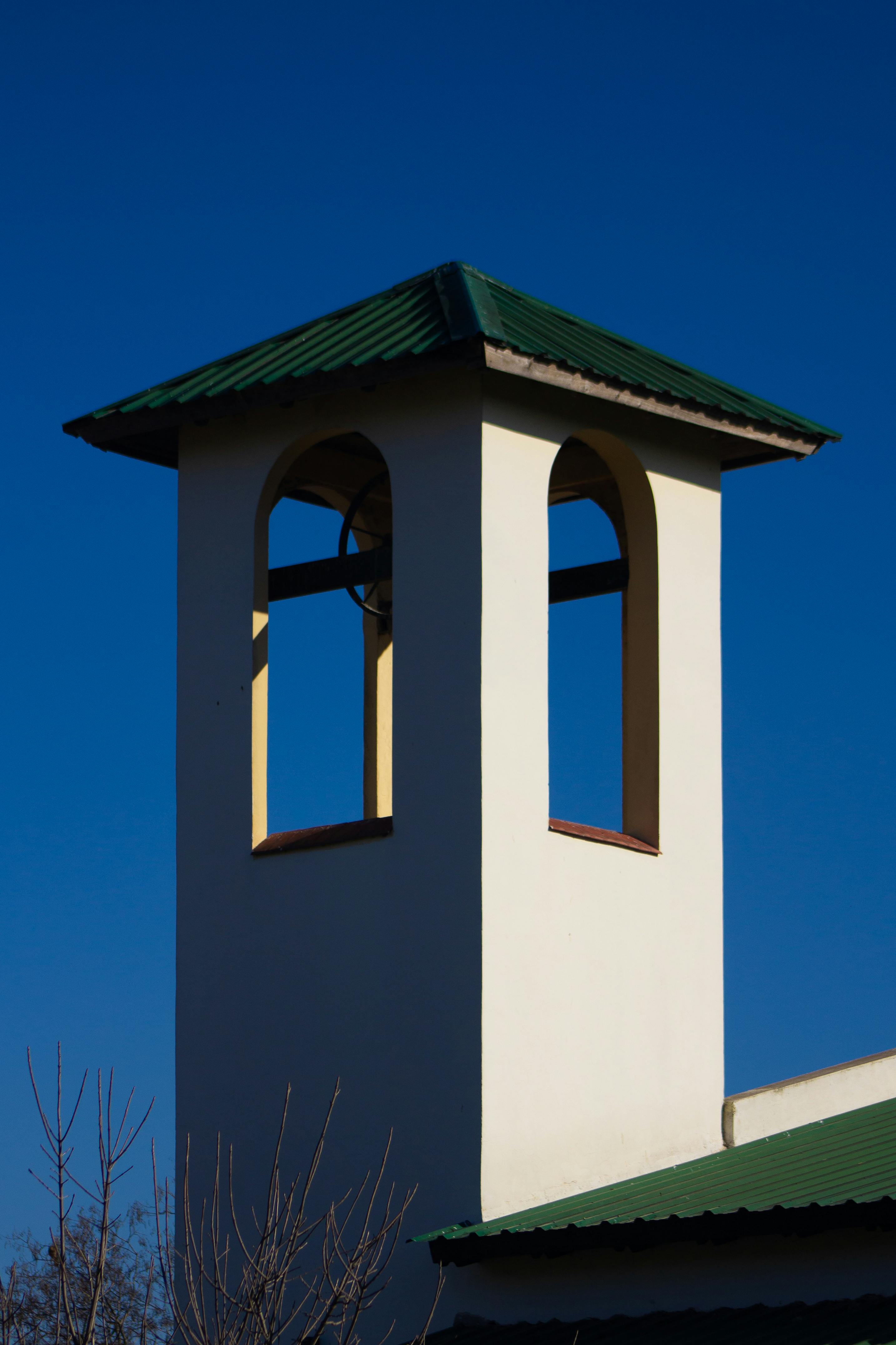 Minimalist shot of a church bell tower with green roof against a vivid blue sky.