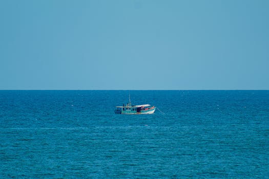 A lone fishing boat navigates the vast calm ocean under a clear blue sky.