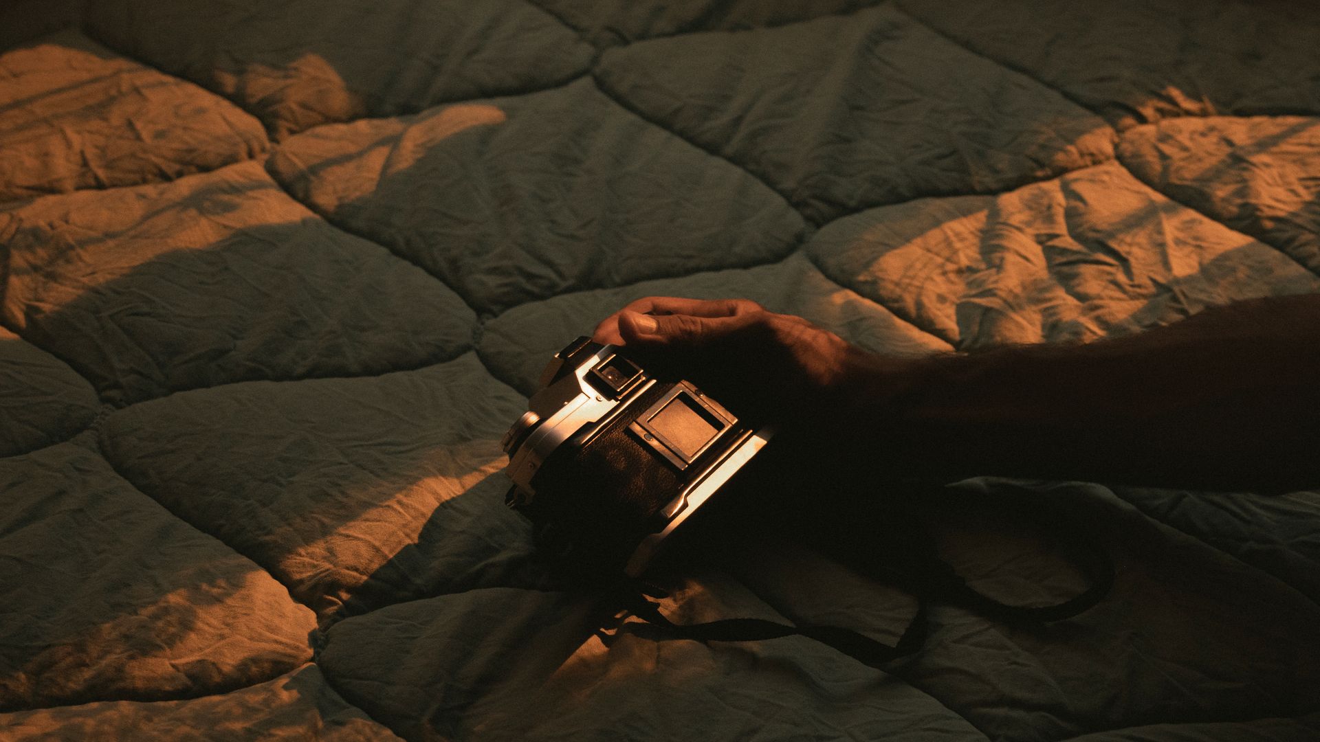 Cozy scene of a hand holding a vintage camera on a quilt under warm lighting.