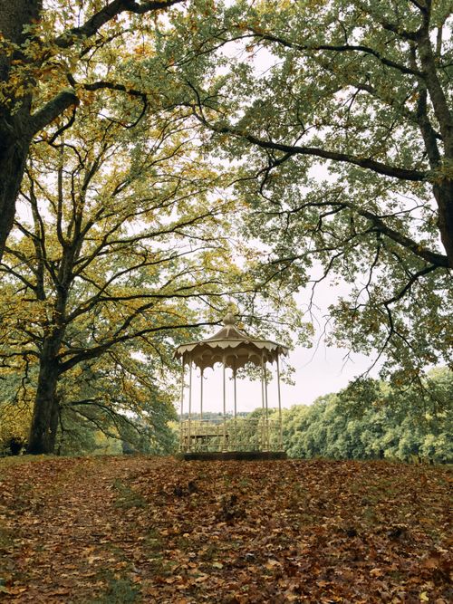 Free Serene autumn scene of a gazebo surrounded by lush trees and fallen leaves in a park. Stock Photo