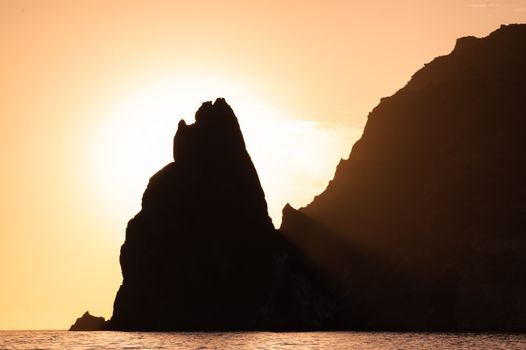 A silhouette of a rock in the ocean at sunset