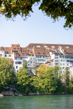 Picturesque buildings along the Rhine River in Basel under a clear summer sky.