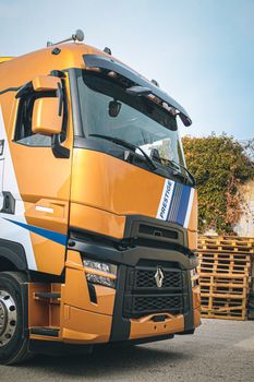 A vibrant golden truck parked outdoors near wooden pallets on a sunny day.