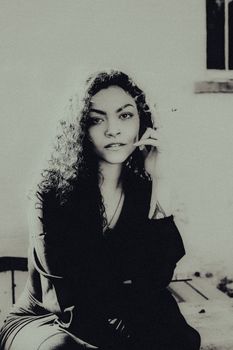 Artistic black and white portrait of a woman sitting with a thoughtful expression.