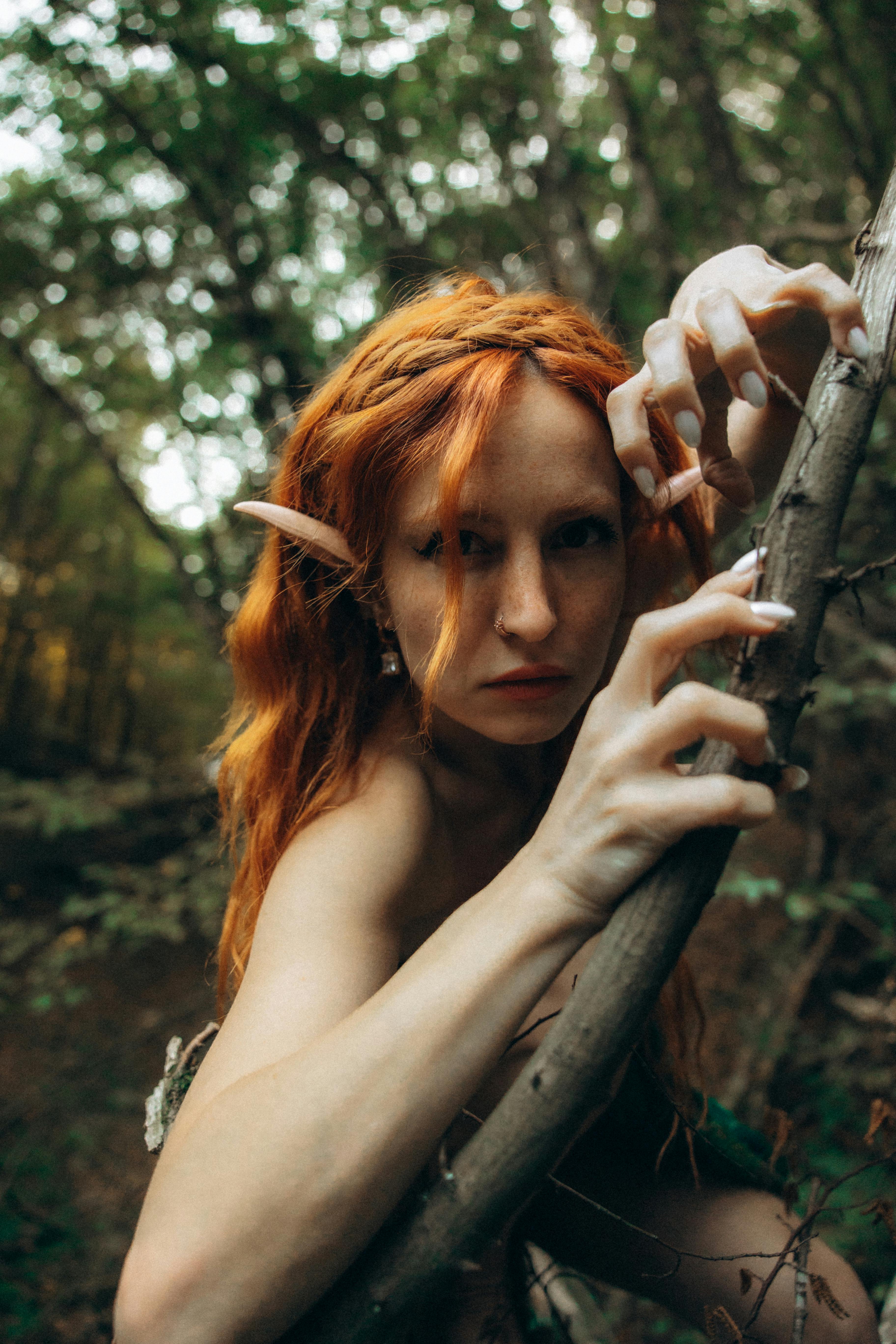 a woman with red hair and green eyes is posing in the woods