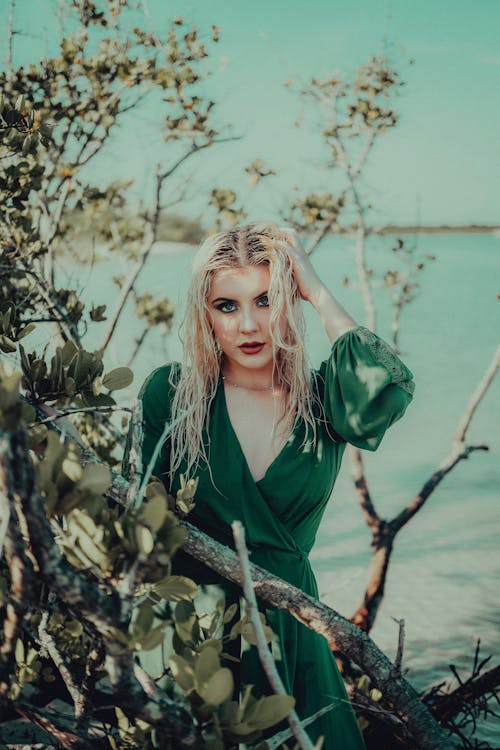 Fixing Hair Blonde Woman in Green Dress in Shrub by Sea