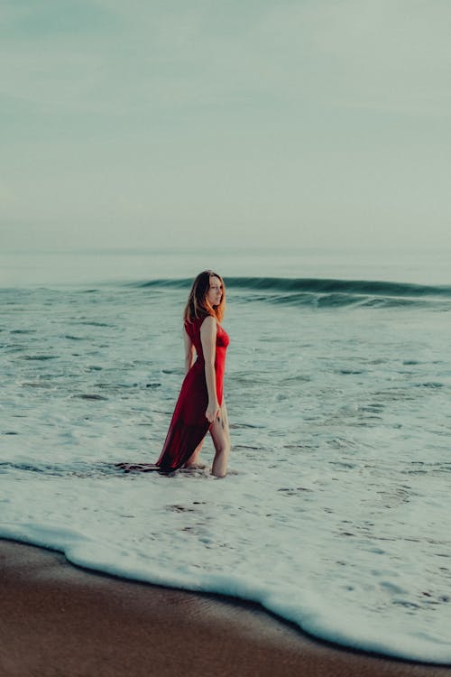 Model in a Long Red Dress with a Slit Wading in the Sea