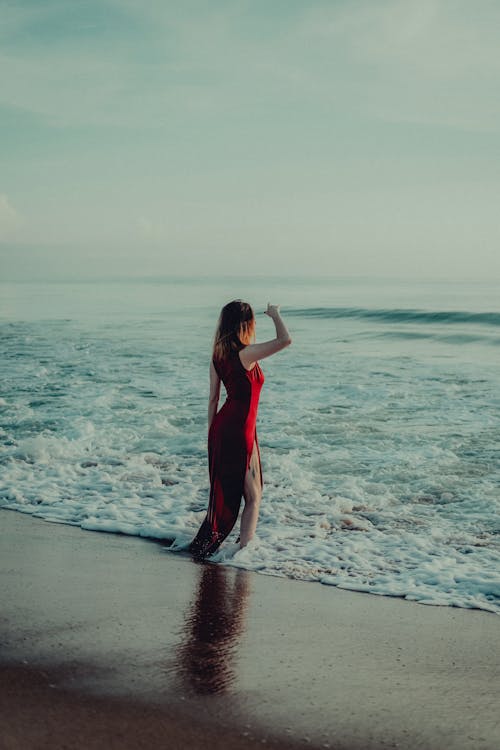Model in a Red Dress with a Slit on a Beach Flooded by the Sea