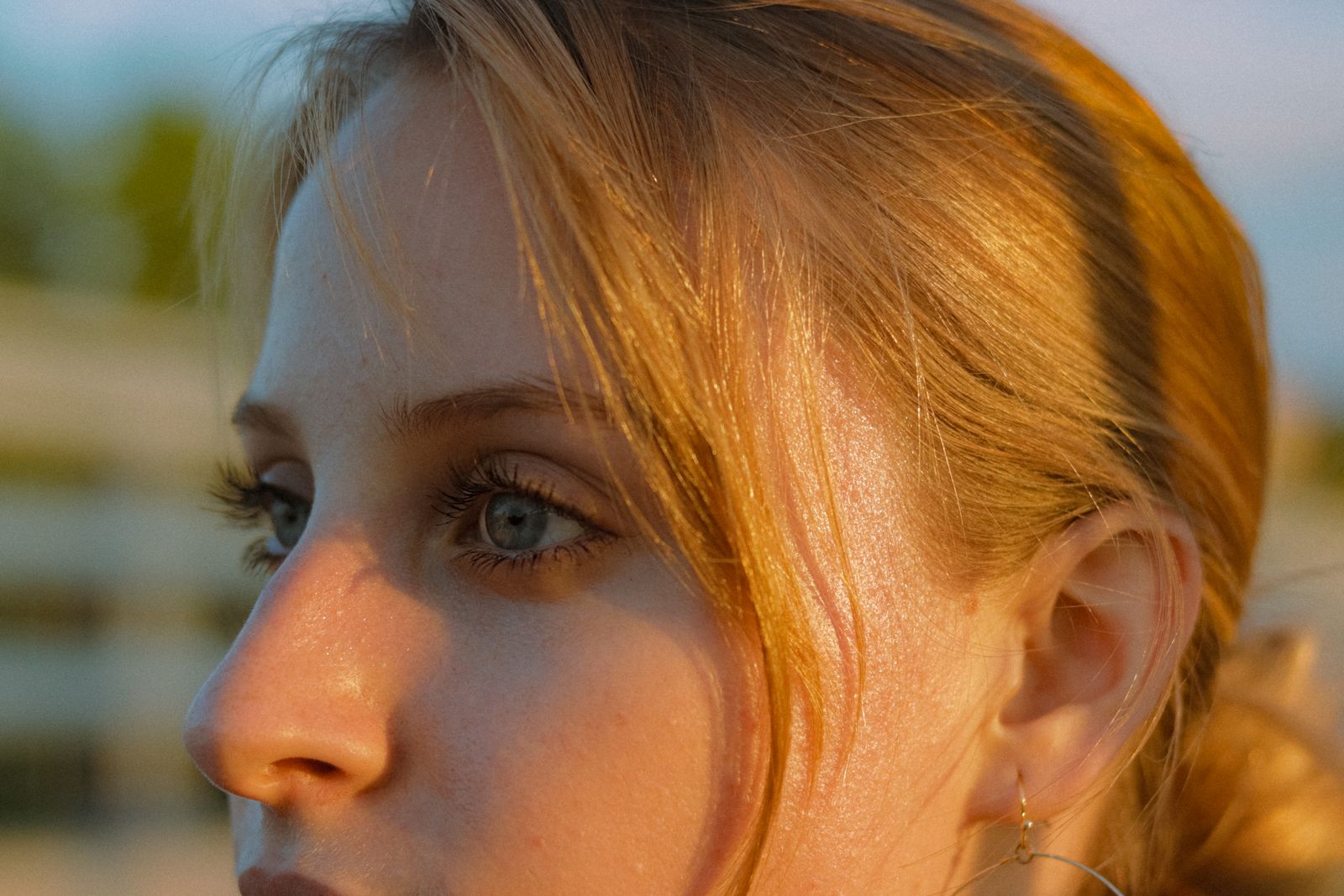 Close-up profile of a blonde woman with warm sunlight falling across her face outdoors.