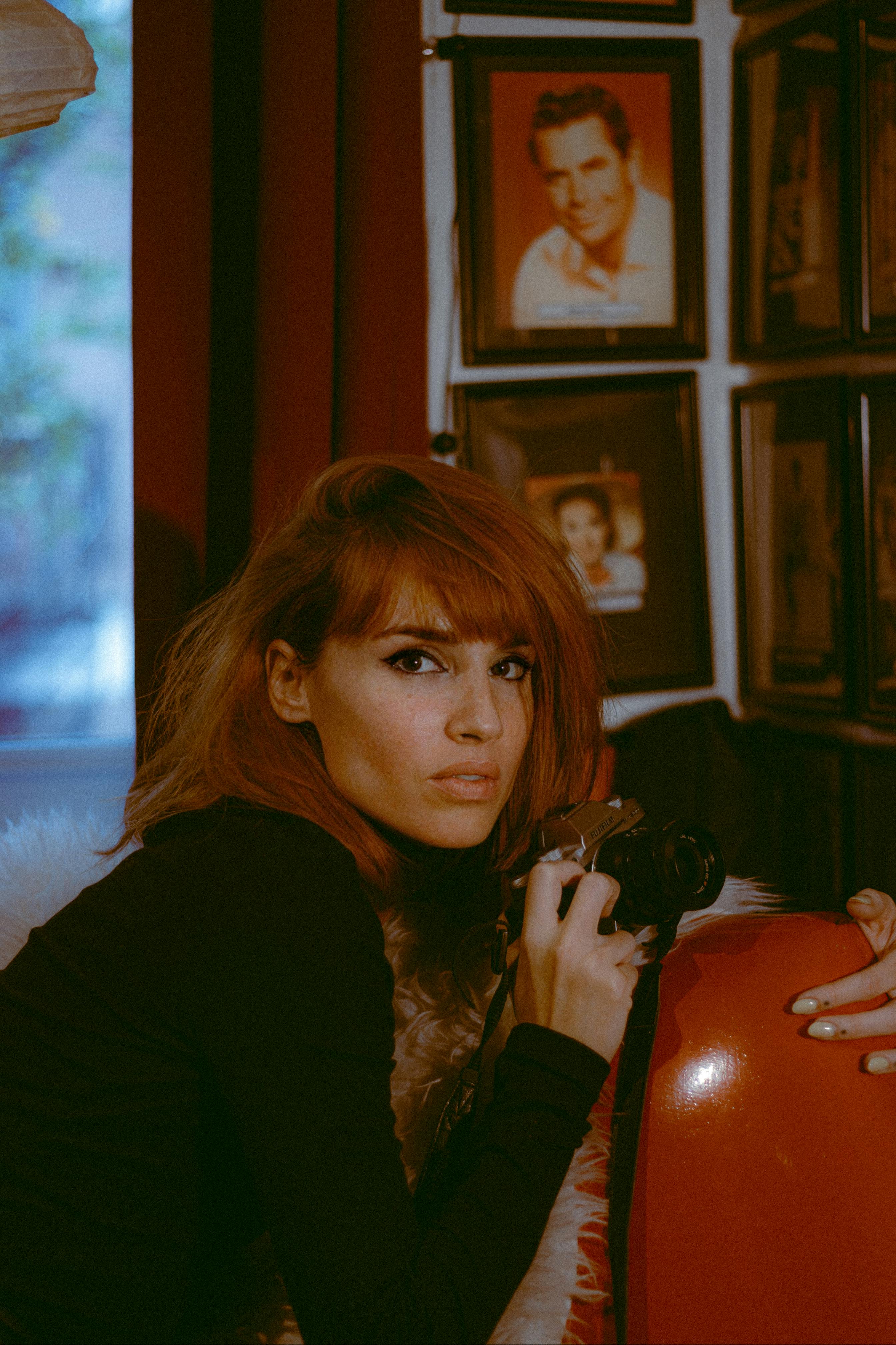 Redhead woman holding a camera in a vintage-inspired setting, capturing a candid moment.