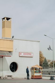 A man stands beside a kiosk at Akköprü station in Ankara with a pigeon in flight.