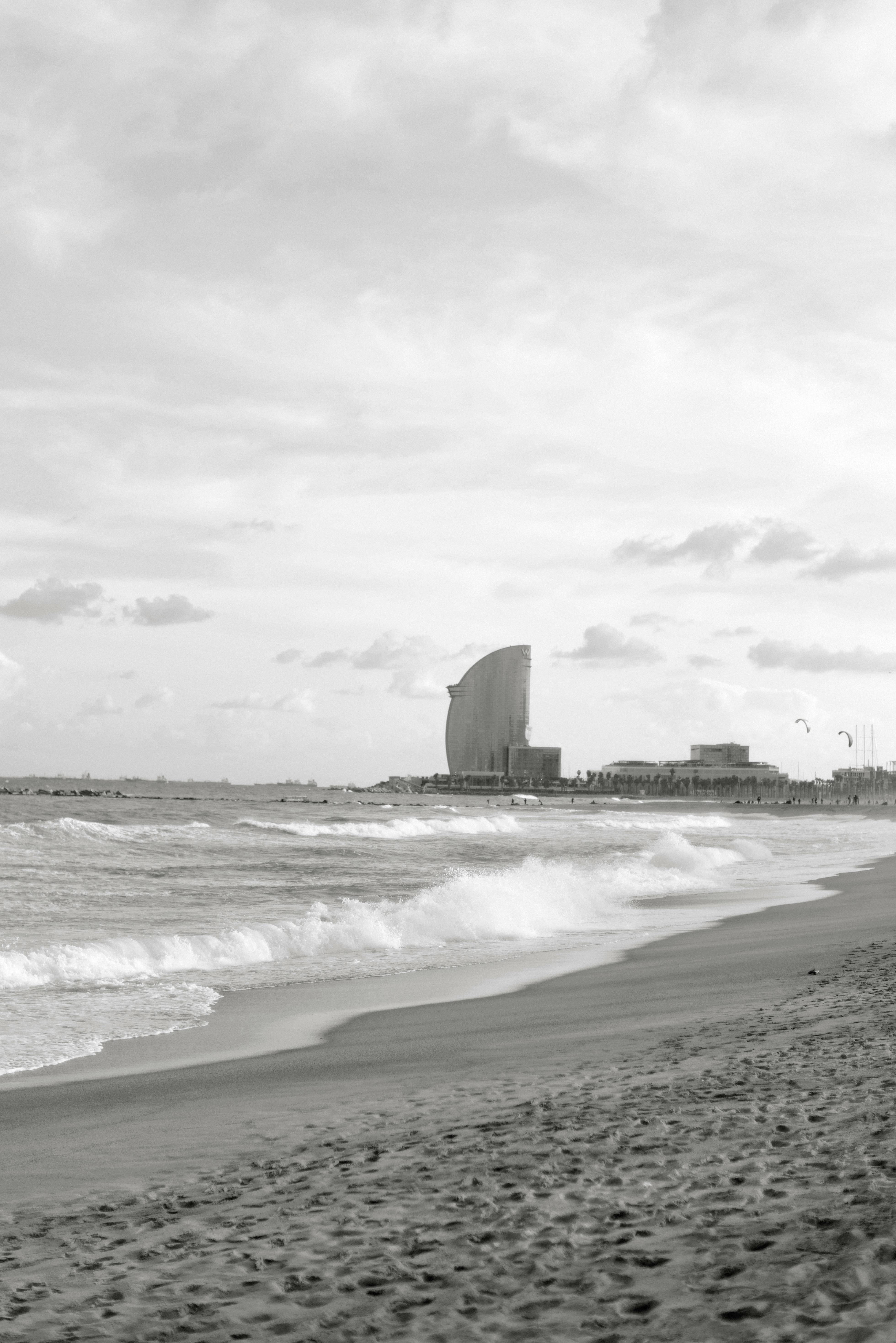 Black and white beach landscape with a prominent building on the horizon.