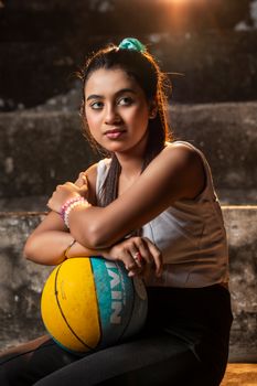 Portrait of a young woman sitting with a basketball, showcasing fashion and sports vibe.