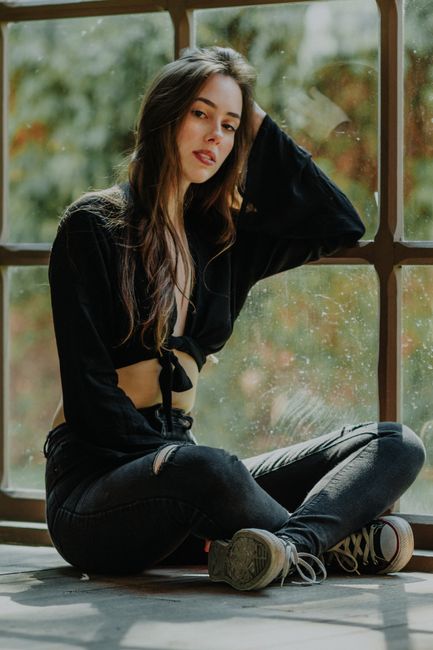 Fashionable young woman sitting by a window in casual attire, exuding confidence and style.