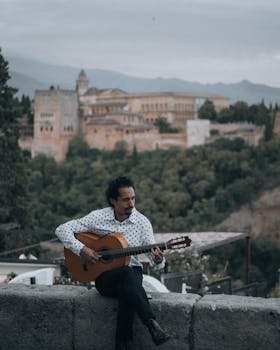 Musician playing acoustic guitar with the historic Alhambra in the background, Granada, Spain.