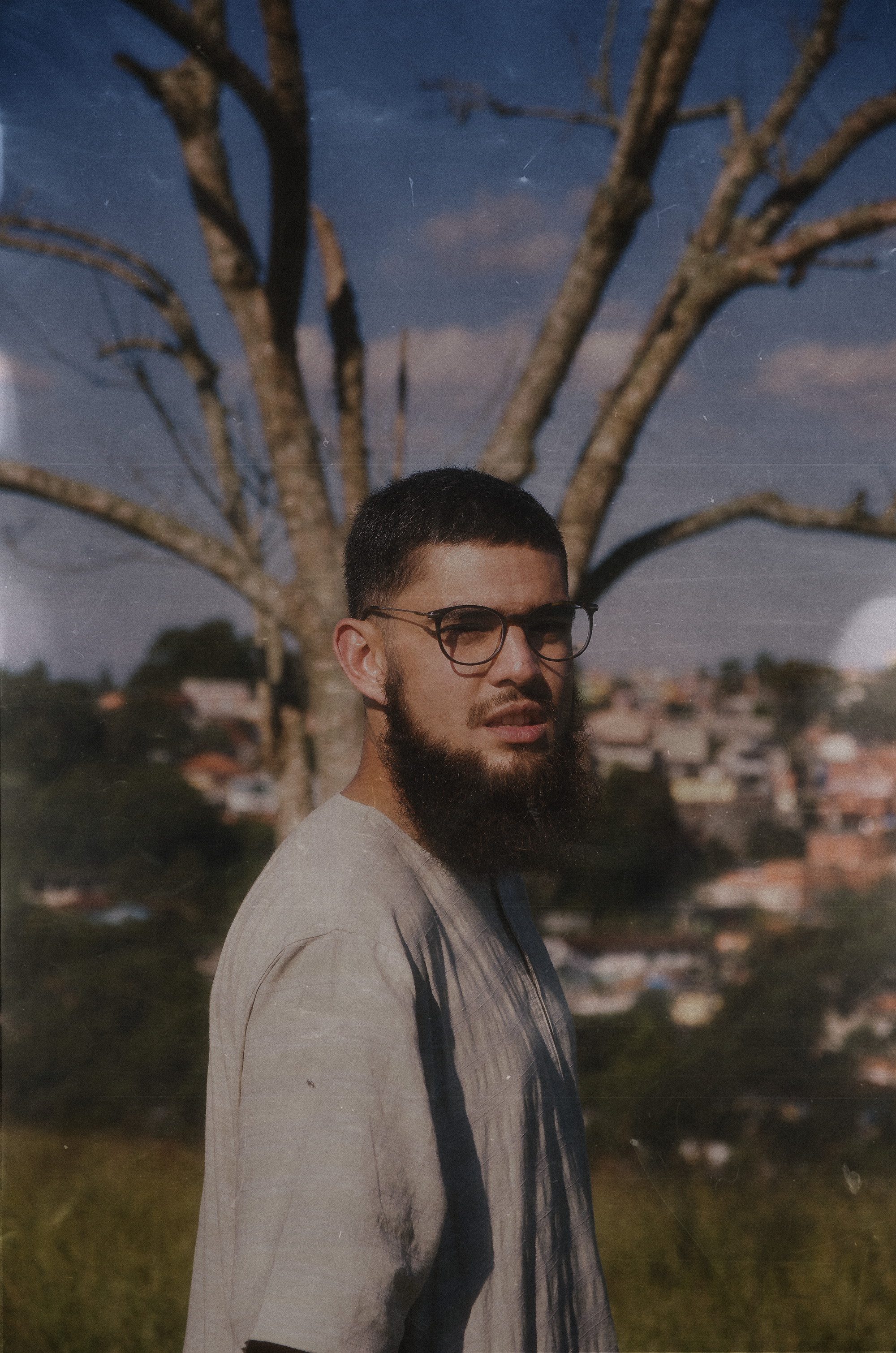 Portrait of a bearded man with eyeglasses standing outdoors in São Paulo, Brazil, on a sunny summer day.
