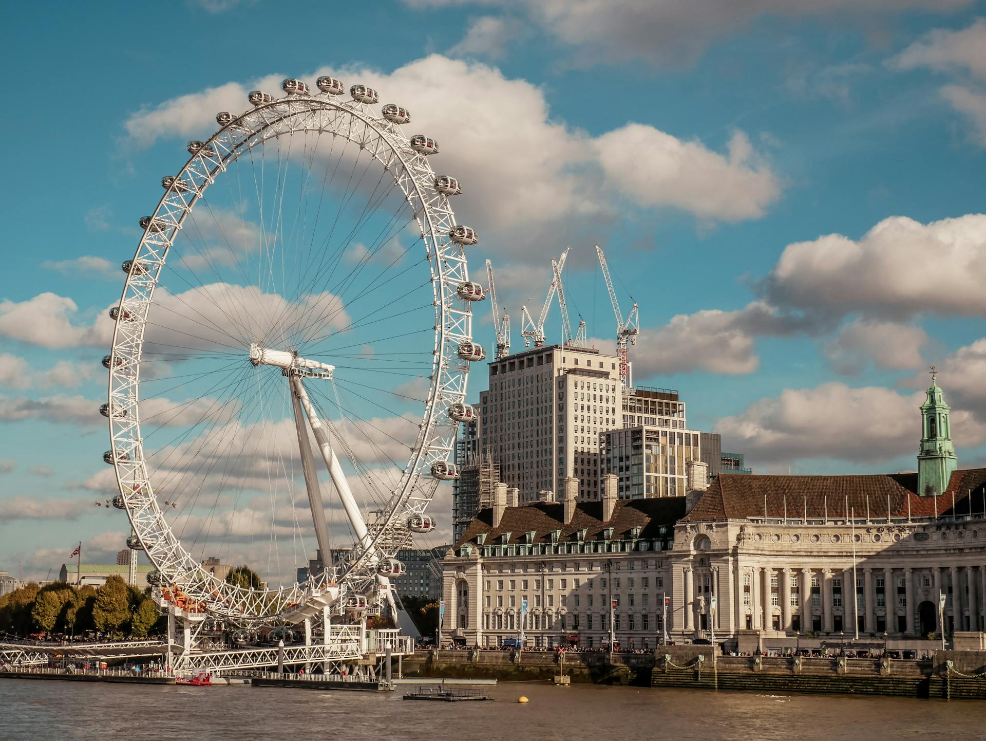 Stunning view of the London Eye with city buildings along the Thames River on a sunny day.