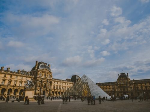 Free A vibrant scene of the Louvre Museum and its iconic glass pyramid in Paris, bustling with visitors. Stock Photo