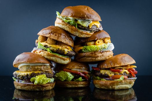 Delicious stack of assorted gourmet cheeseburgers photographed against a dark background.