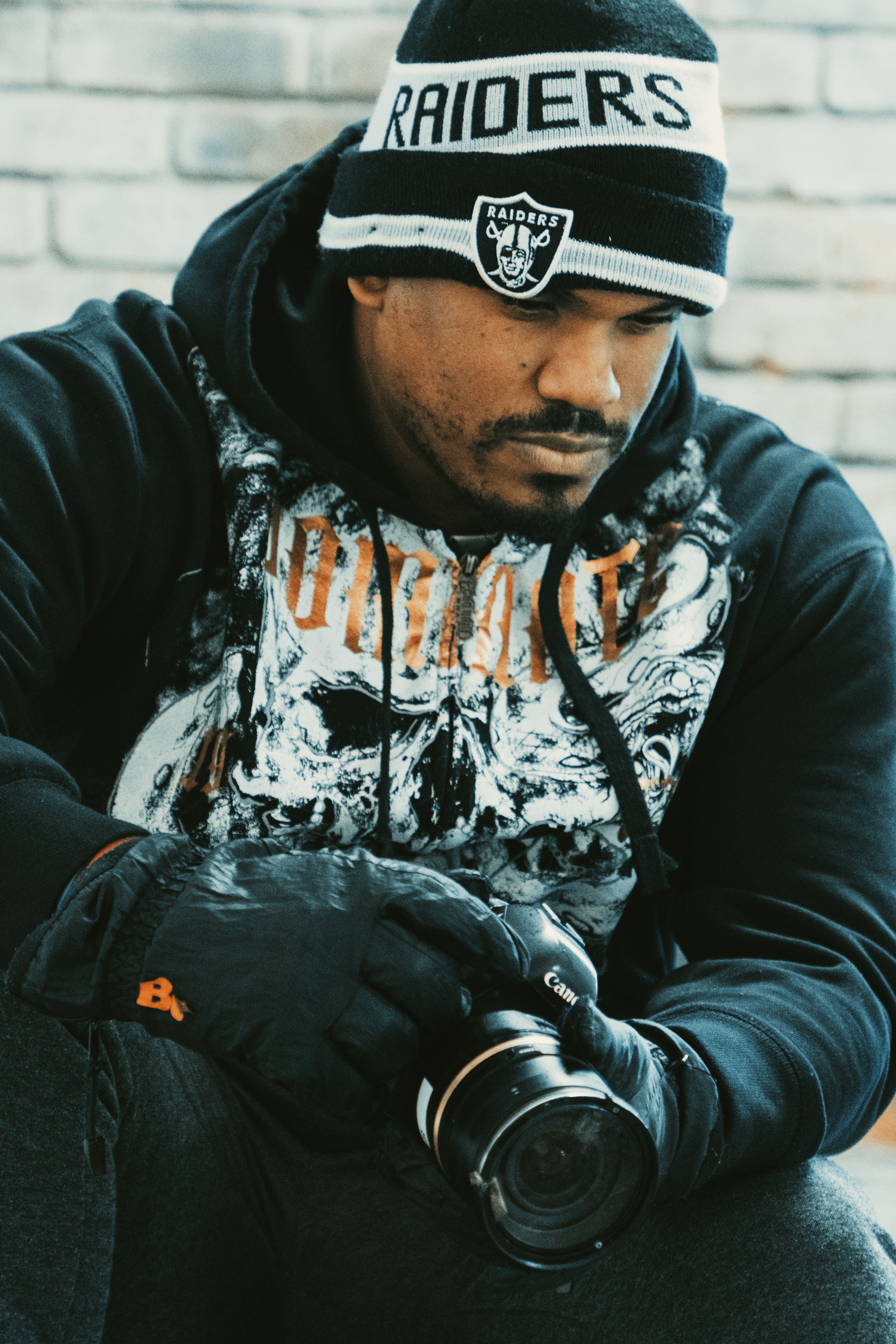 A thoughtful man wearing winter attire holds a camera, lost in thought.