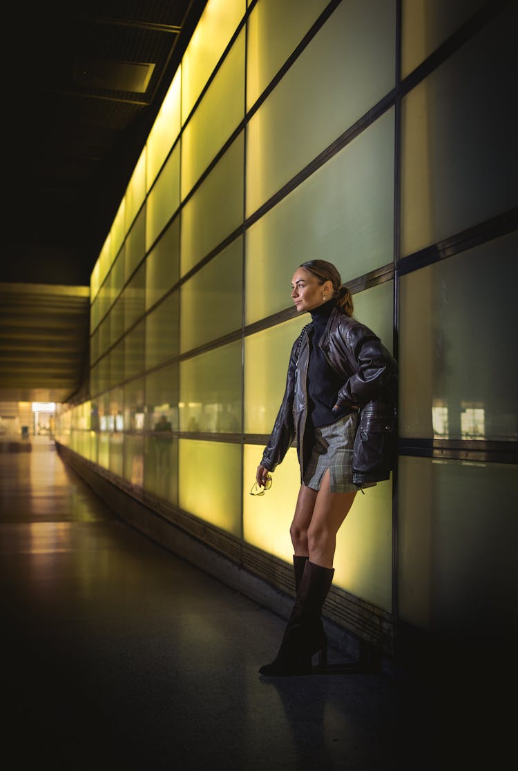 Young Woman Posing Near Glass Building Wall At Night