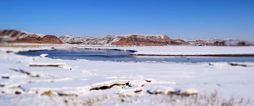 Body of Water Surrounded by Snow Ground Under Blue Sky