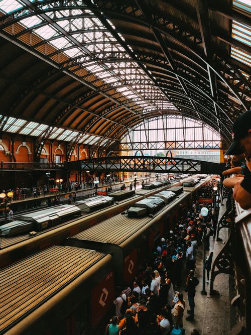 Free Vibrant scene inside a historical train station with crowded platforms and a distinctive arched roof. Stock Photo